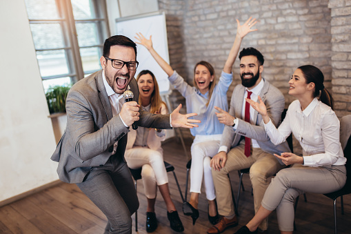 Business people making team training exercise during team building seminar singing karaoke.